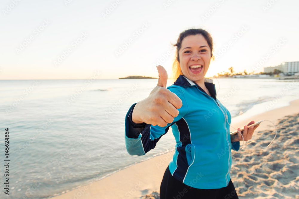 Concept of sport, fitness, healthy lifestyle and running - Motivated sporty woman doing thumbs up success gesture after outdoors workout at the beach Concept of sport, fitness, healthy lifestyle and running - Motivated sporty woman doing thumbs up success gesture after outdoors workout at the beach