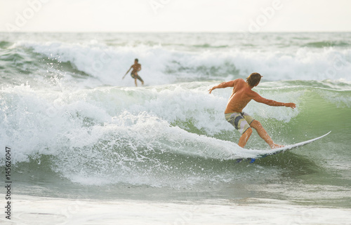 The surfer with tanned body  rolls on the waves at sunset. photo