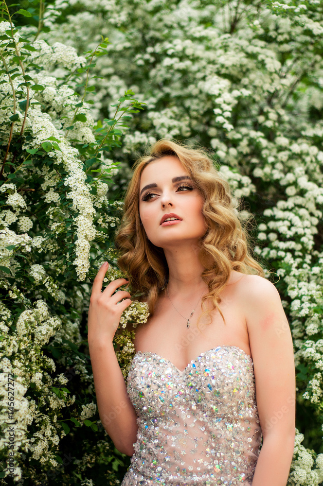 Girl in evening cocktail dress on a spring in the middle among flowering bushes and trees beautiful smiling Girl in evening cocktail dress on a spring in the middle among flowering bushes and trees beautiful smiling