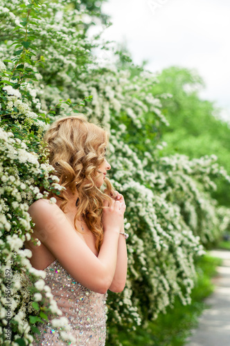 Girl in evening cocktail dress on a spring in the middle among flowering bushes and trees beautiful smiling