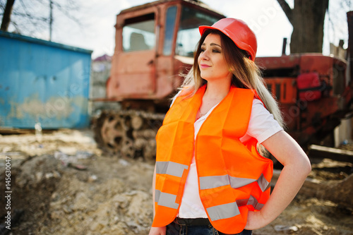 Canvas Print Engineer builder woman in uniform waistcoat and orange protective helmet against bulldozer
