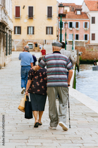 Elderly couple walking arm in arm through the ancient streets of Venice in Italy.