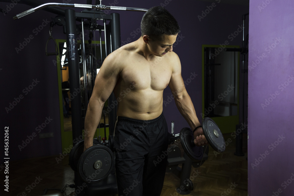Naklejka premium Muscular Young Man Doing Heavy Weight Exercise For Shoulders In Gym