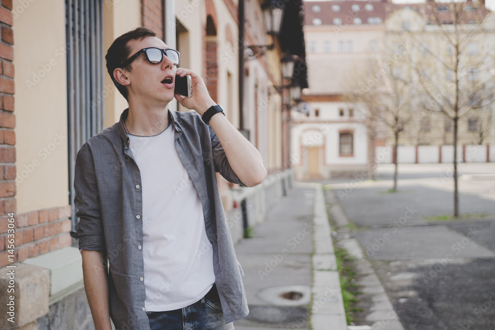 Happy young hipster man walking on the street and talking on phone