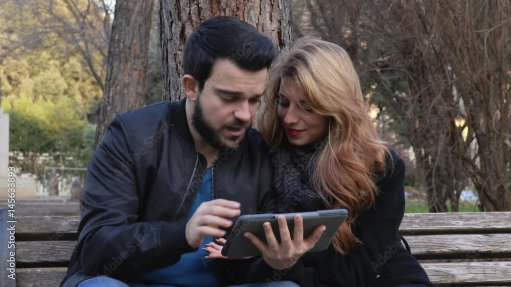 sweet happy couple on a bench at the park using tablet sweet happy couple on a bench at the park using tablet