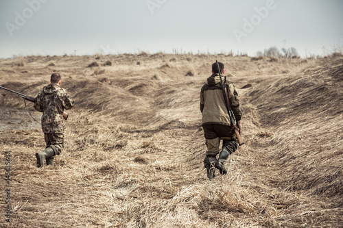 Hunters running across dry rural field during hunting