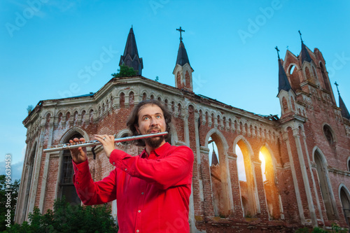 Musician in red playing the flute near an old castle at sunset