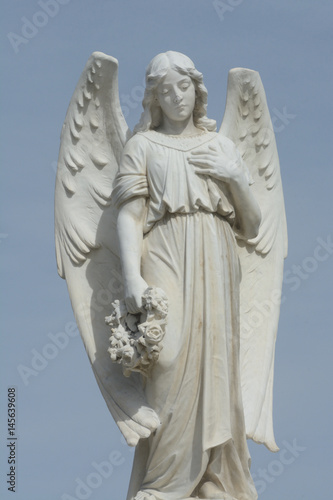 Gravestone memorial with angel holding wreath of flowers against overcast sky