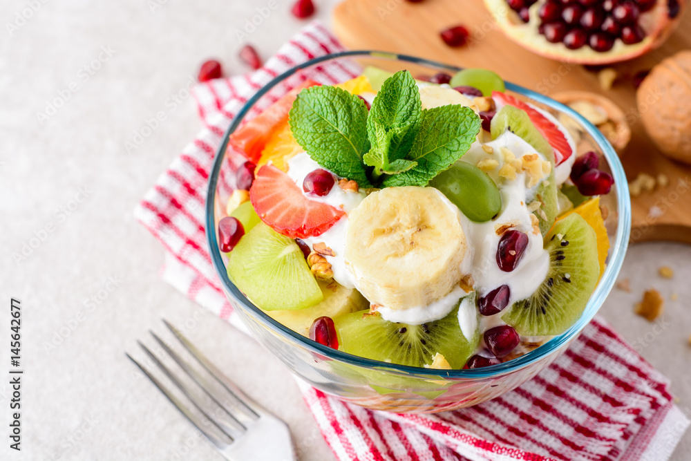 Fresh fruit salad with yogurt and walnuts in glass bowl on stone background. Fresh fruit salad with yogurt and walnuts in glass bowl on stone background.