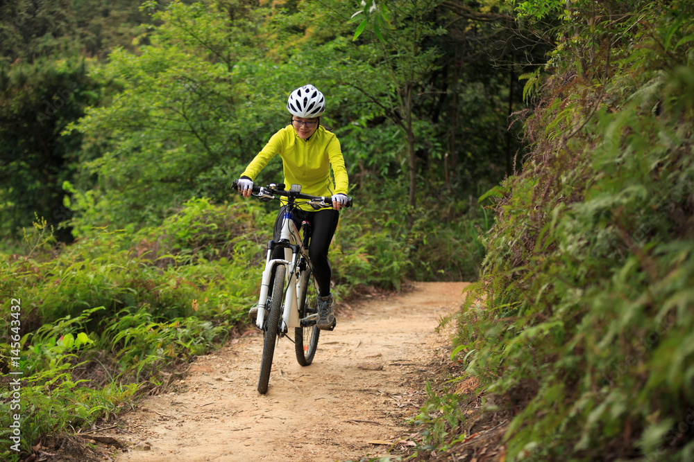 Young woman cyclist cycling mountain bike on forest trail