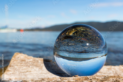 Glaskugel auf Baumstamm am See mit Segelboot im Hintergrund