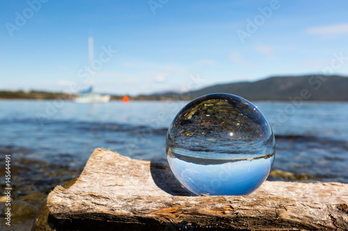 Glaskugel auf Baumstamm am See mit Segelboot im Hintergrund © rosifan19