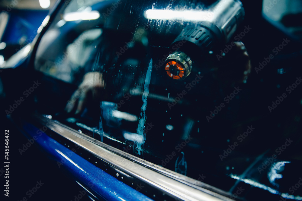 Φωτογραφία Master installs a tint film for the car glass with a hairdryer and spatula with glare of light