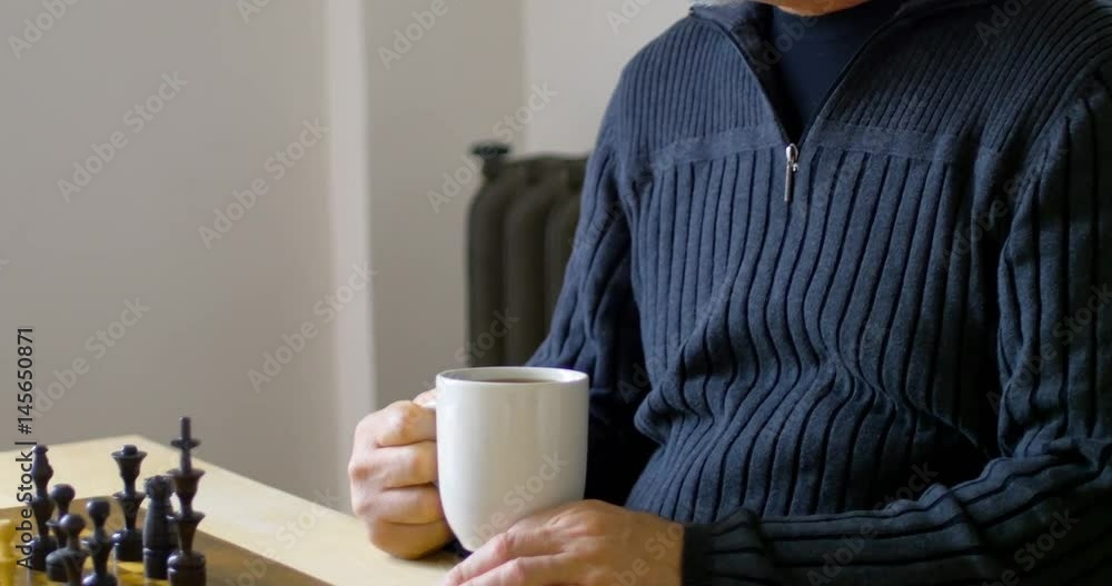 Man having coffee while playing chess in living room Man having coffee while playing chess in living room