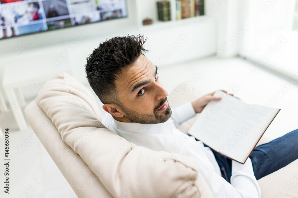Obraz premium Young confident man reading book at modern home