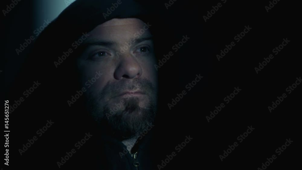 Man with thoughtful hood in the dark opens his eyes and looks at the light Man with thoughtful hood in the dark opens his eyes and looks at the light