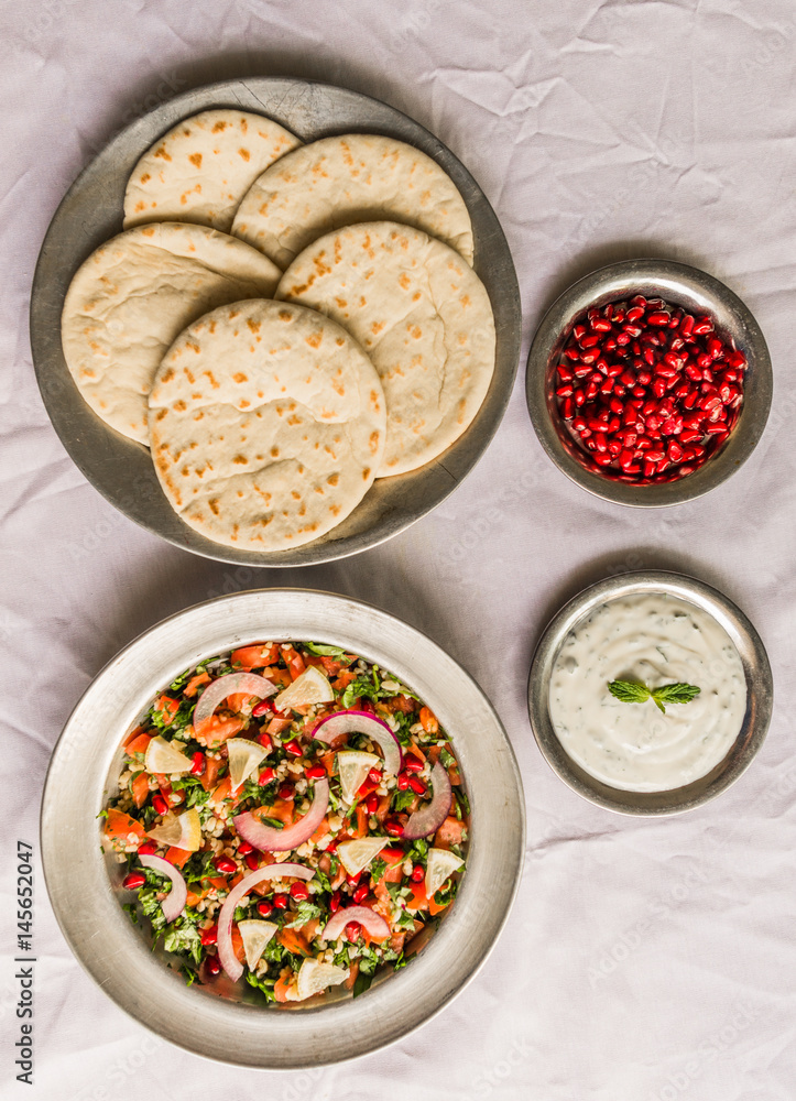 Tabbouleh salad and Arab pita bread with pomegranate seeds and white sour cream sauce against white background. Selective focus.