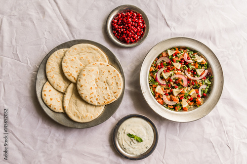 Tabbouleh salad and Arab pita bread with pomegranate seeds and white sour cream sauce against white background. Selective focus.
