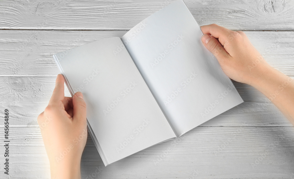 Female hands holding blank brochure on white wooden table Female hands holding blank brochure on white wooden table