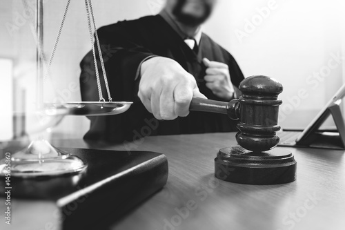 justice and law concept.Male judge in a courtroom with the gavel,working with smart phone and digital tablet computer with brass scale on wood table,black and white