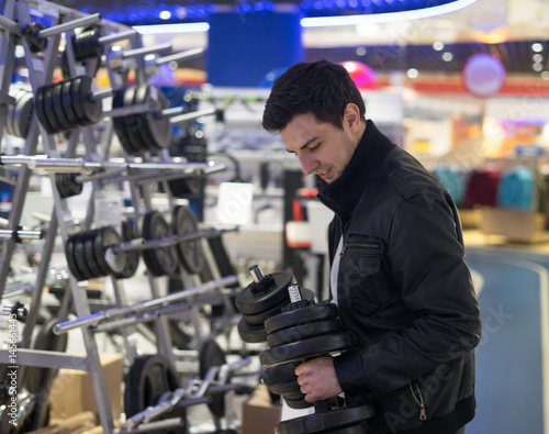 portrait of young male customer choosing dumbbells at supermarket store