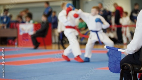 Martial art competitions - coach-judge with blue flag looking at karate teenager's fighting
