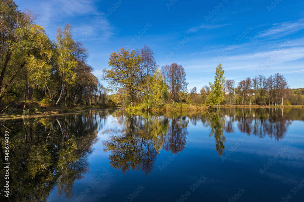 Reflection of small trees in a lake under a blue sky with intermittent clouds