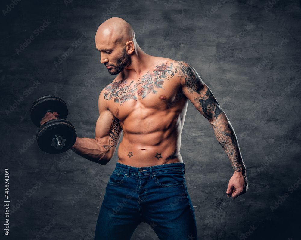 Positive shaved head shirtless male dressed in a jeans holds the dumbbell.