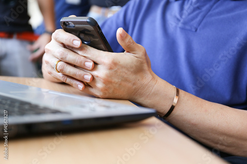 Man is holding mobile phone on hands in front of laptop on wooden desk