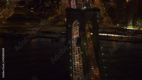 AERIAL HELI SHOT, NO VISIBLE TRADEMARKS Automobile traffic moving across the iconic Brooklyn bridge lit up with lights on magical summer night in New York City. People commuting from work at rush hour