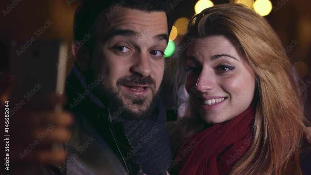 Smiling couple doing funny selfie at night in the city,close up Smiling couple doing funny selfie at night in the city,close up