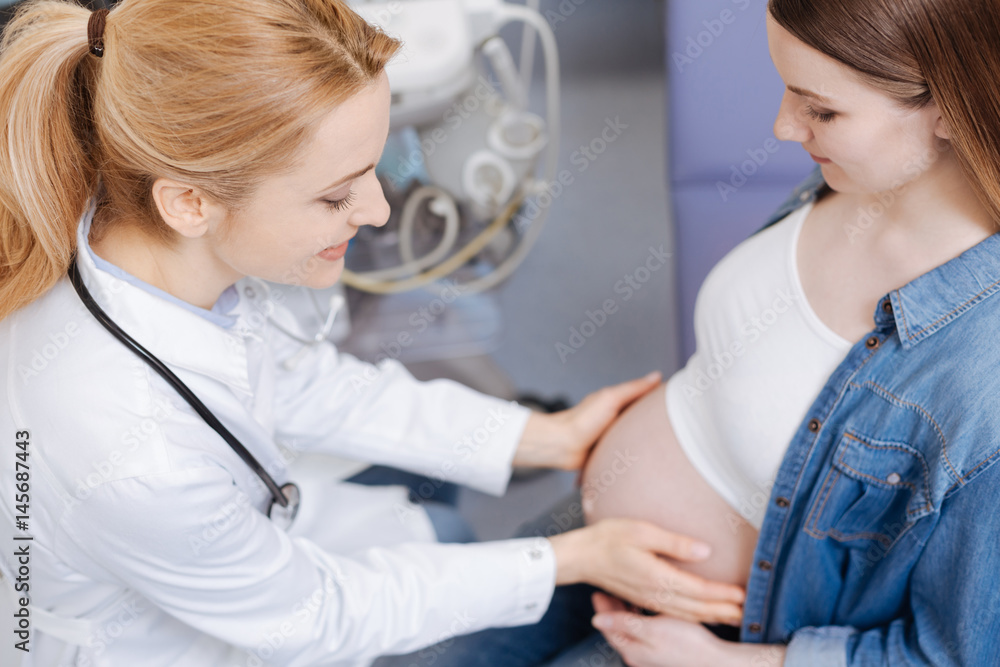 Kind obstetrician examining pregnant belly in the clinic