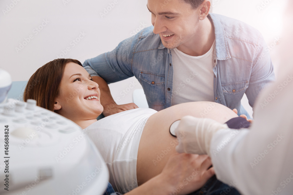 Helpful young husband supporting pregnant wife in the sonography cabinet Helpful young husband supporting pregnant wife in the sonography cabinet