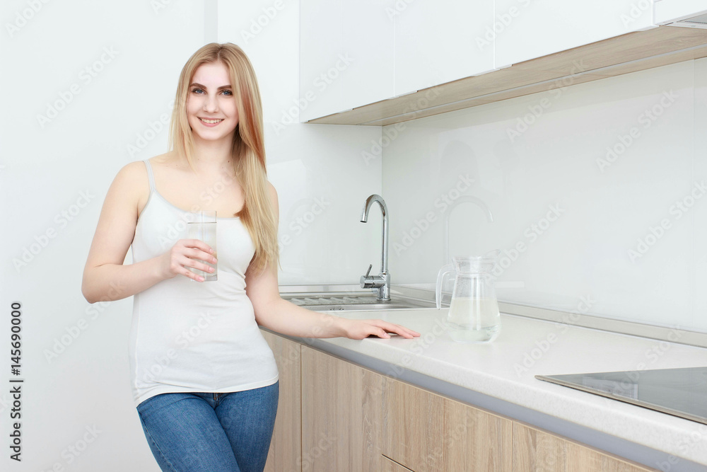 Beautiful young woman holds a glass with water on kitchen