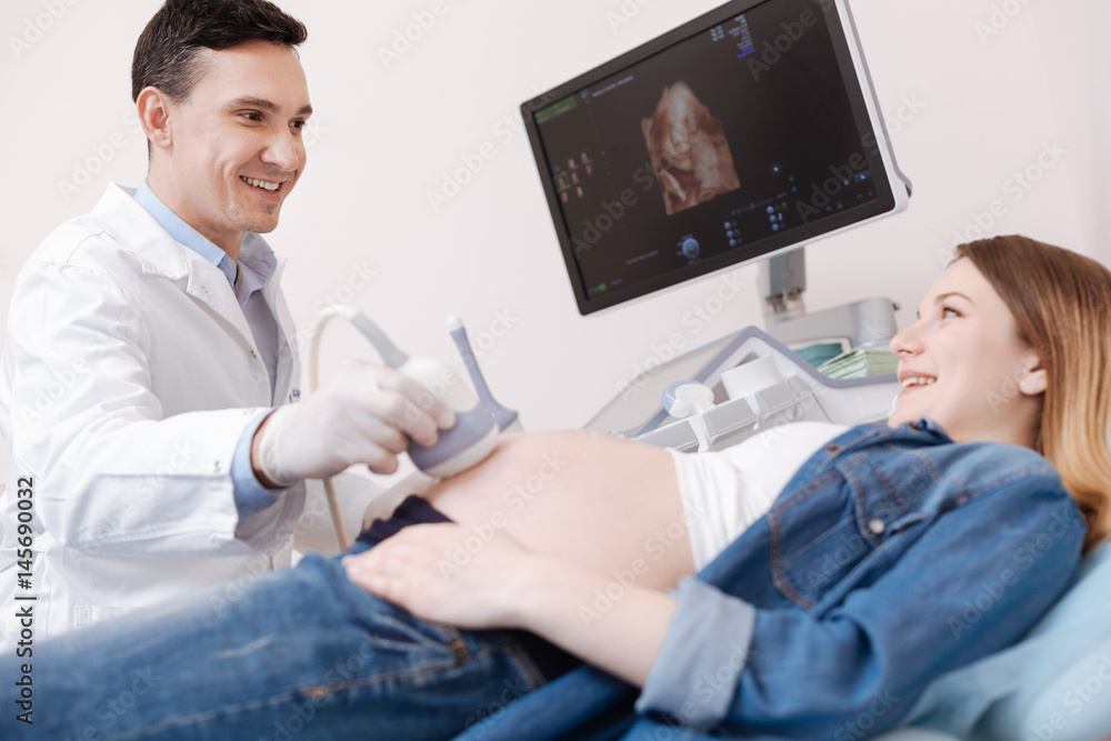 Smiling gynecologist providing ultrasonic pregnant patient monitoring at work Smiling gynecologist providing ultrasonic pregnant patient monitoring at work