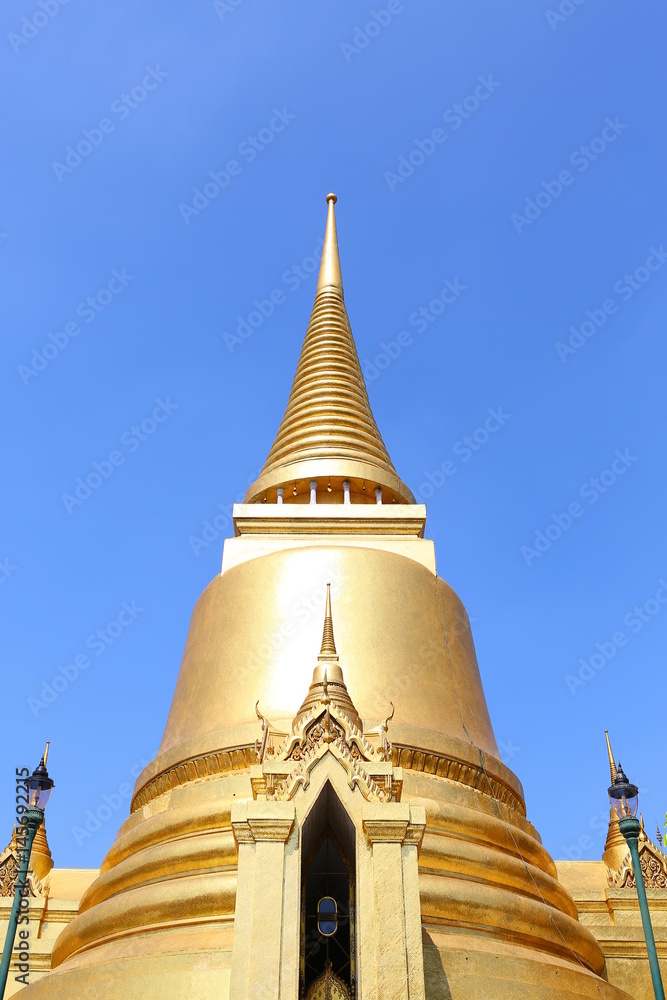 Naklejka premium Golden pagoda against blue sky background on display at wat pra kaew in Bangkok, Thailand.