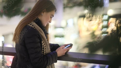 Fabuluous ukrainian girl chatting with her friend by smartphone in shoppng mall, unfocused leaves on the front plan, Steady cam, slow mo shot photo