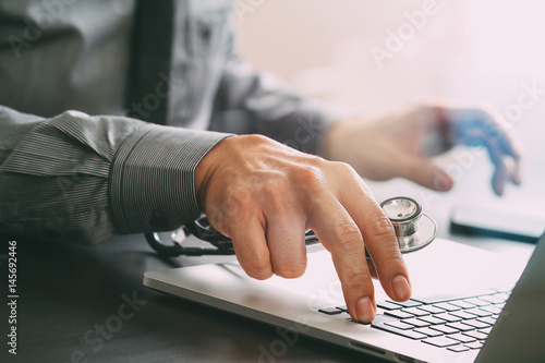 close up of smart medical doctor working with laptop computer and stethoscope on dark wooden desk