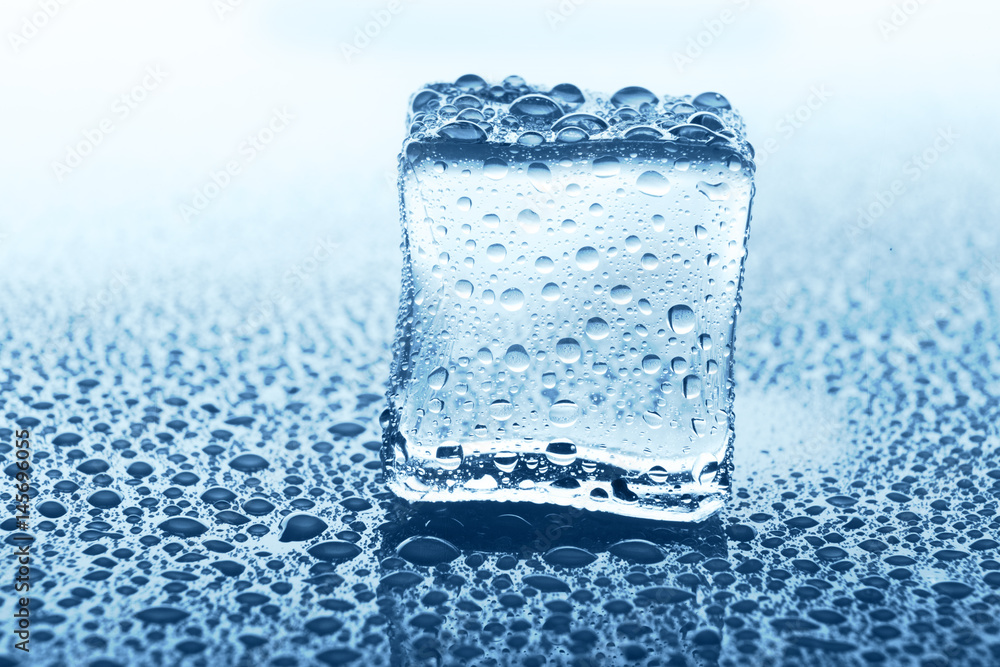 Transparent ice cube with reflection on blue glass with water drops Transparent ice cube with reflection on blue glass with water drops
