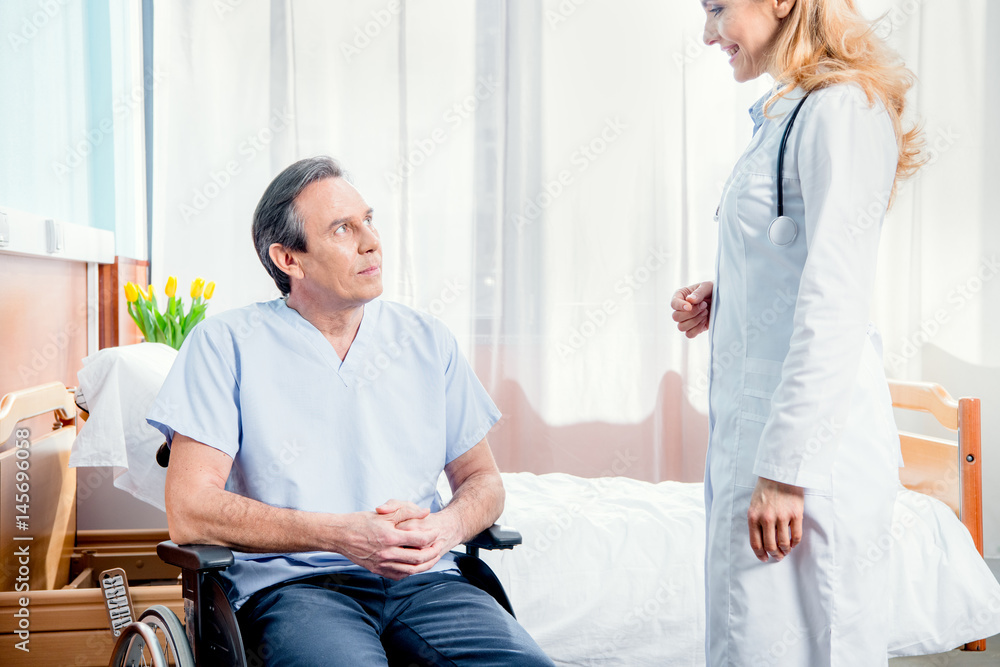Obraz premium elderly man sitting in wheelchair and doctor standing near him in hospital