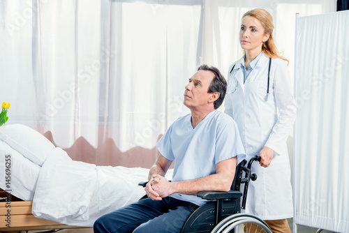 elderly man sitting in wheelchair and doctor standing near him in hospital