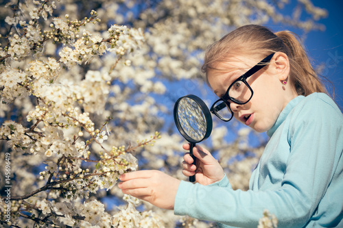 Happy little girl exploring nature with magnifying glass at the day time