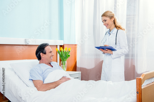 middle aged patient lying on bed and doctor with diagnosis standing near him in hospital