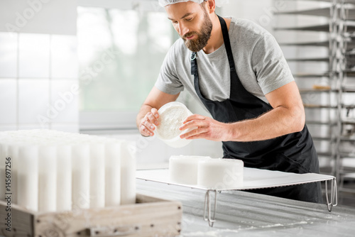 Canvastavla Handsome cheese maker in uniform forming cheese into molds at the small producin
