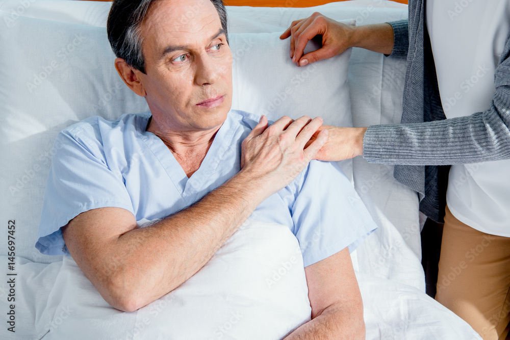 Obraz premium wife visiting her middle aged husband and holding hands in hospital