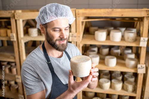 Tableau sur toile Handsome cheese maker checking the aging process of the goat cheese standing at