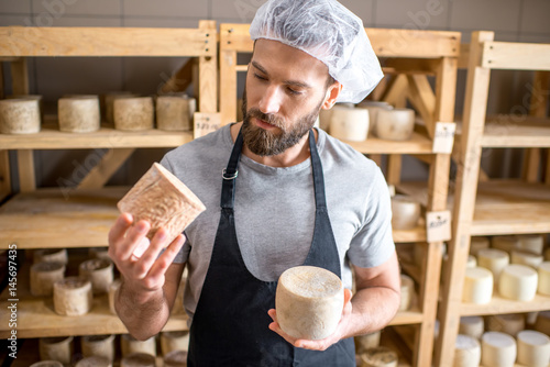 Cuadro en lienzo Handsome cheese maker checking the aging process of the goat cheese standing at