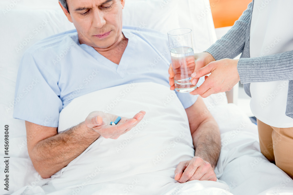 man taking medicines and woman holding glass of water near by man taking medicines and woman holding glass of water near by