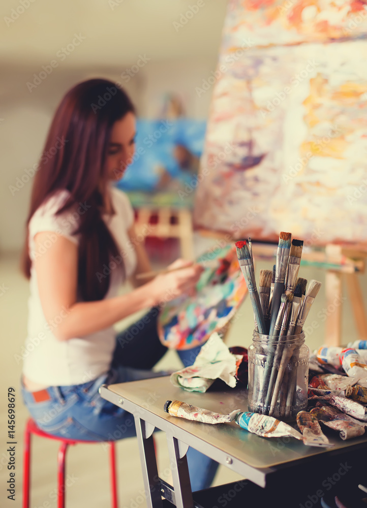 Fototapeta premium Female Artist Working On Painting In Studio. Background image, selective focus on foreground