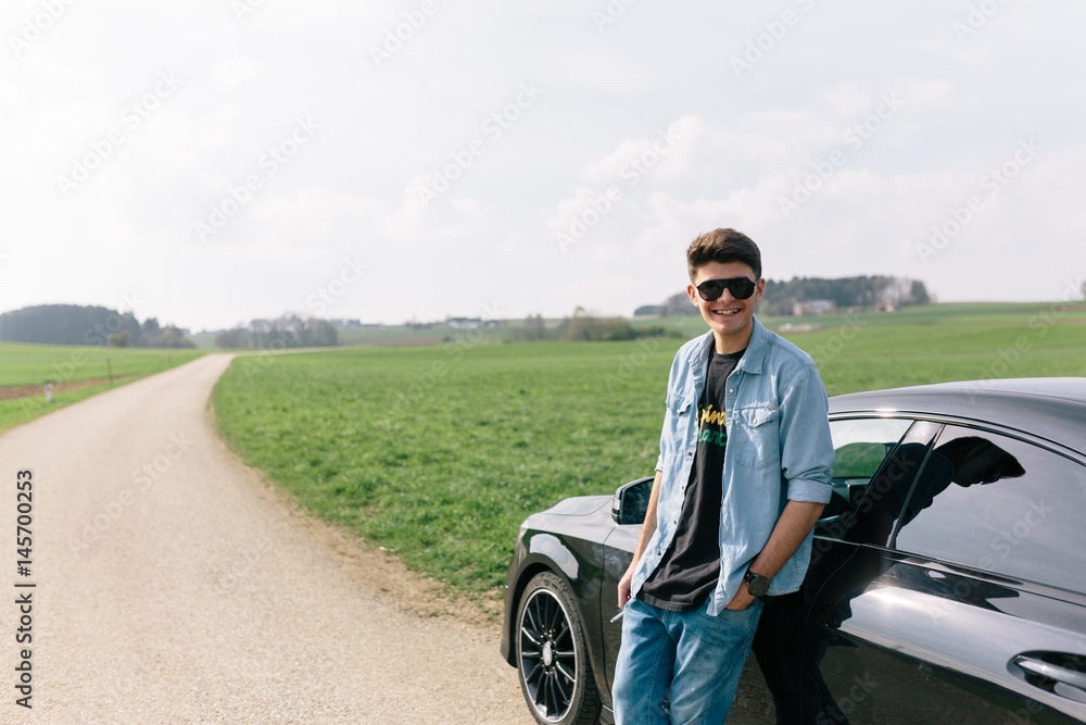 Young man leaning on car on country road
